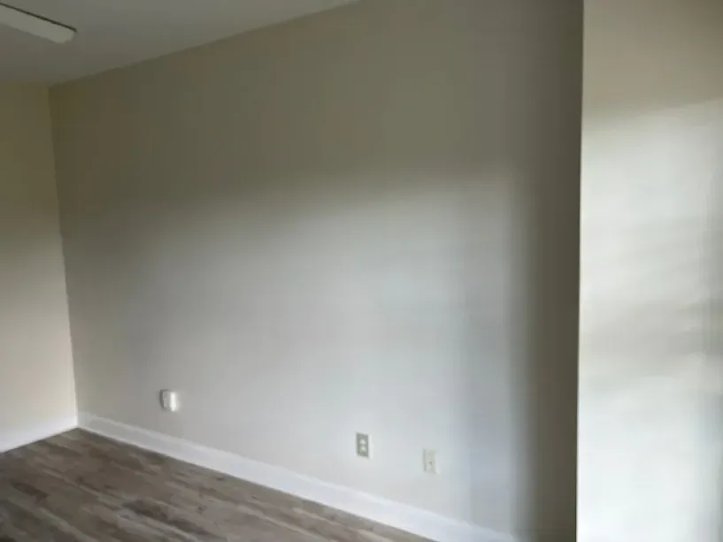 An empty room with a white wall and wooden floor.