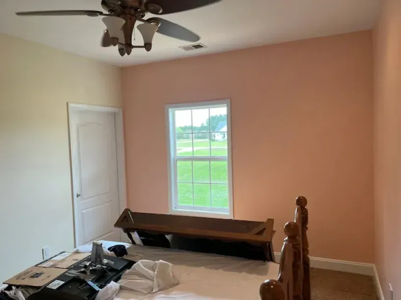 A bedroom with pink walls and a ceiling fan.