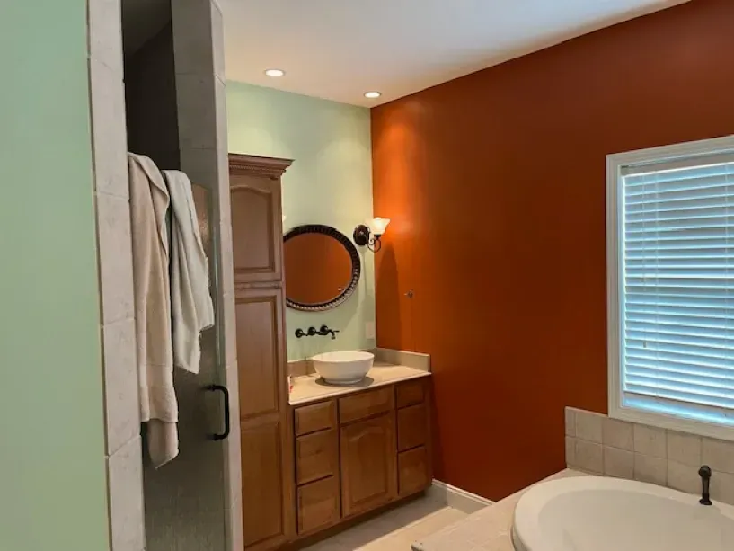 A bathroom with a tub , sink , mirror and orange walls.