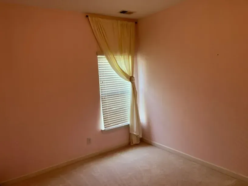 An empty bedroom with pink walls and a window with blinds.