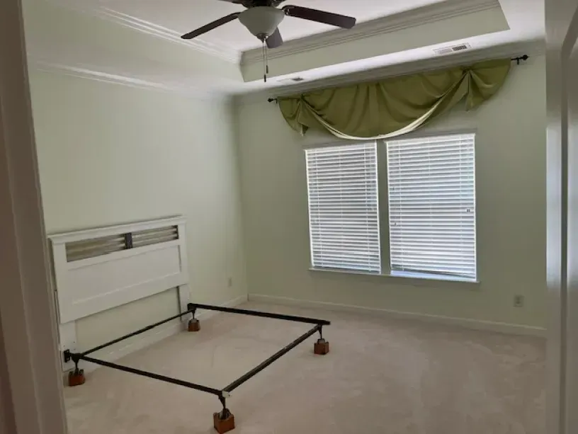An empty bedroom with a bed frame and a ceiling fan.