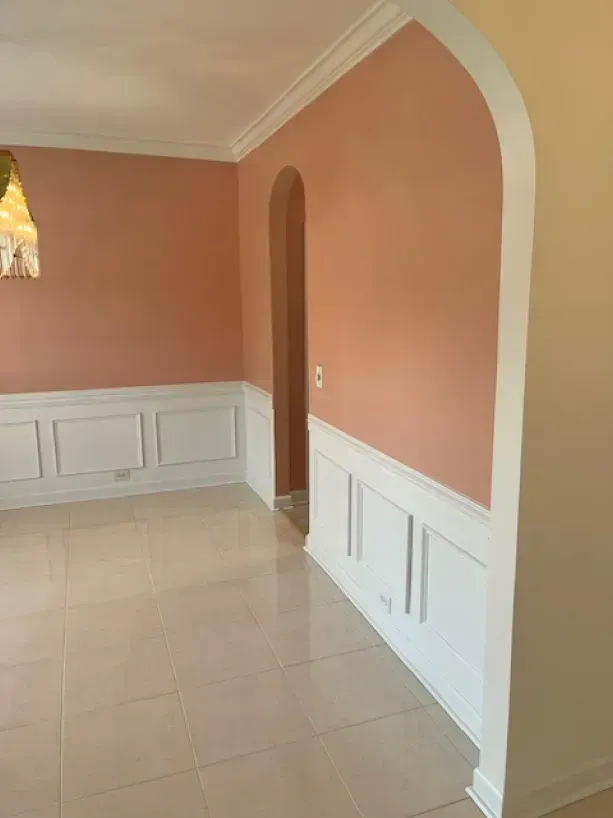 An empty dining room with pink walls and white trim.