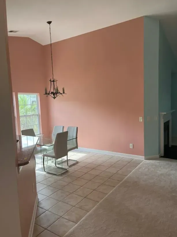 A dining room with pink walls and a chandelier hanging from the ceiling.
