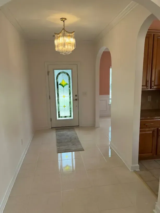 A hallway with a stained glass door and a chandelier hanging from the ceiling.