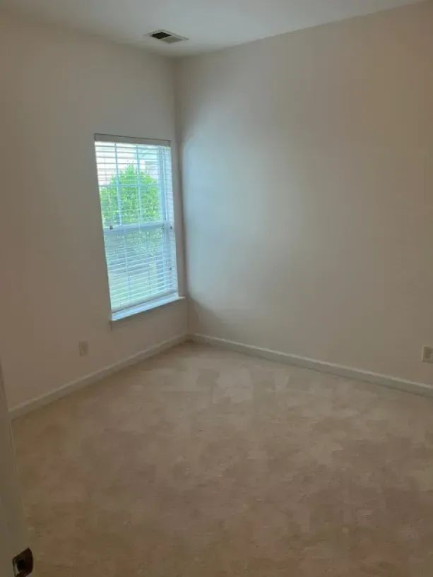 An empty bedroom with a window and a carpeted floor.