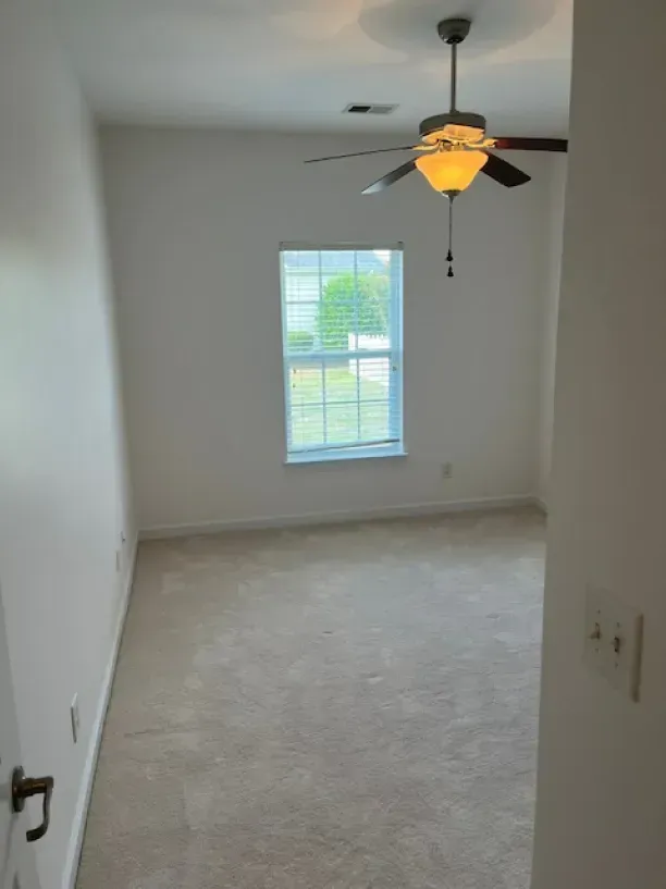 An empty bedroom with a ceiling fan and a window.
