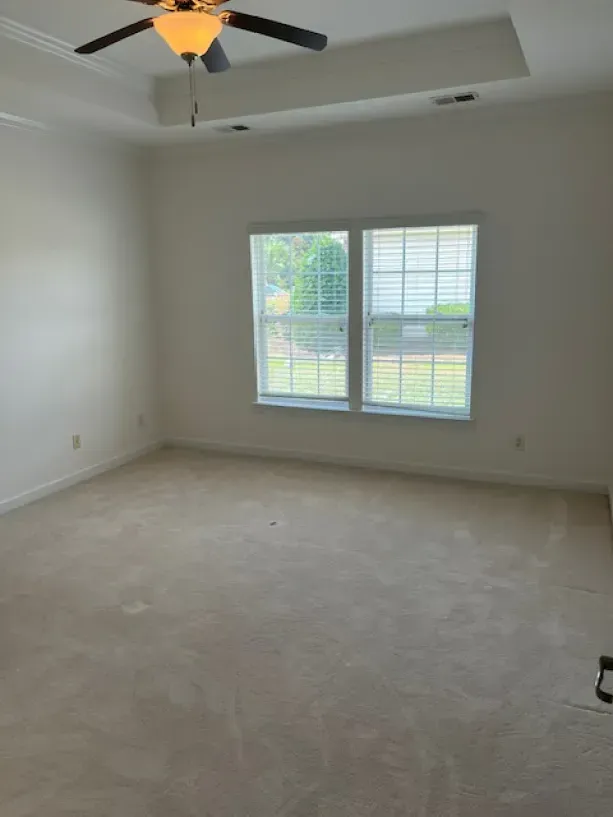 An empty living room with a ceiling fan and two windows.