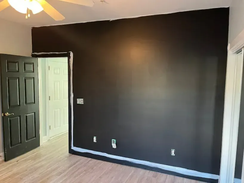A bedroom with a black wall and a ceiling fan.