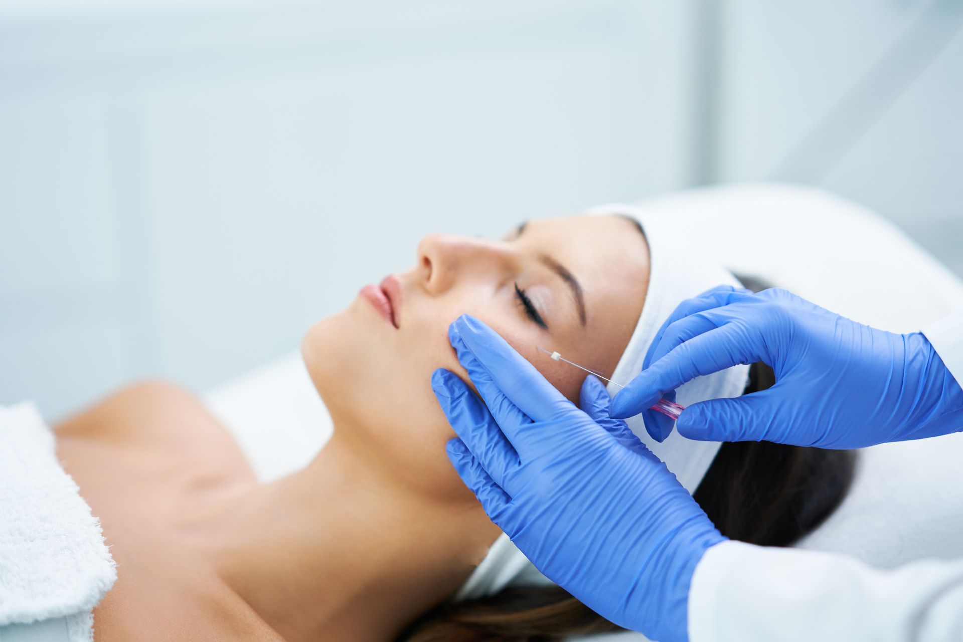 Woman receiving facial injections. A medical professional in blue gloves administers the procedure.