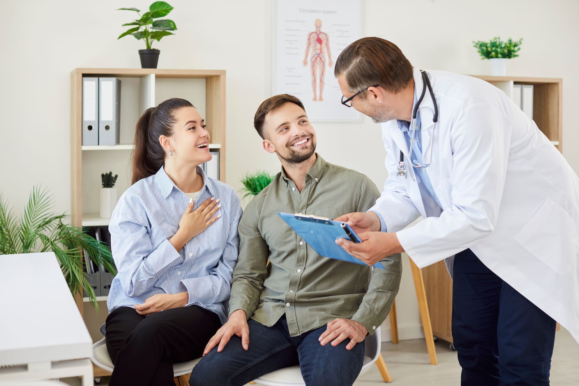 Couple happily listening to a doctor holding a clipboard in an office setting.