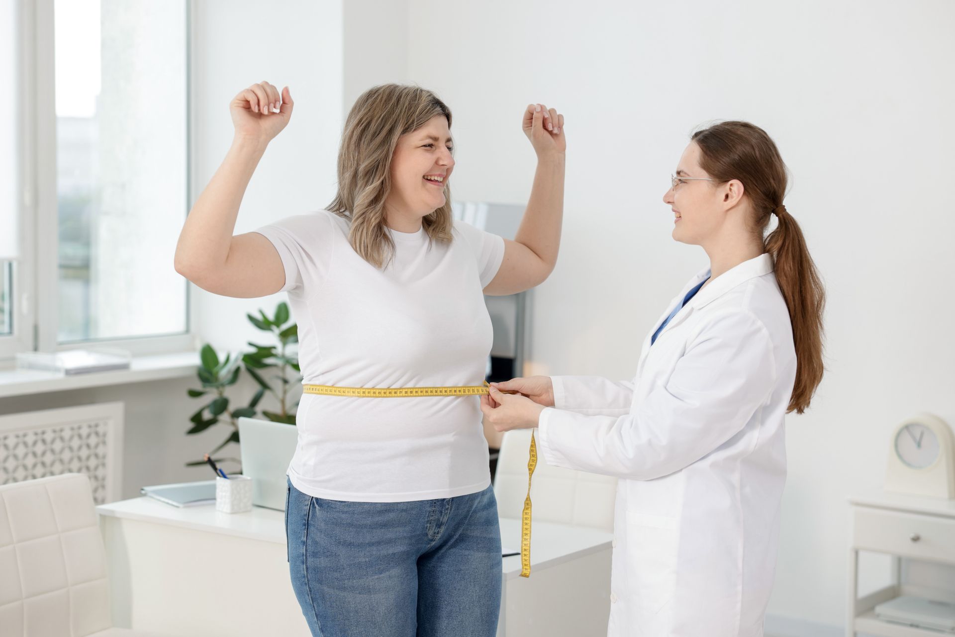 Woman celebrates with arms raised as doctor measures her waist in a bright office.