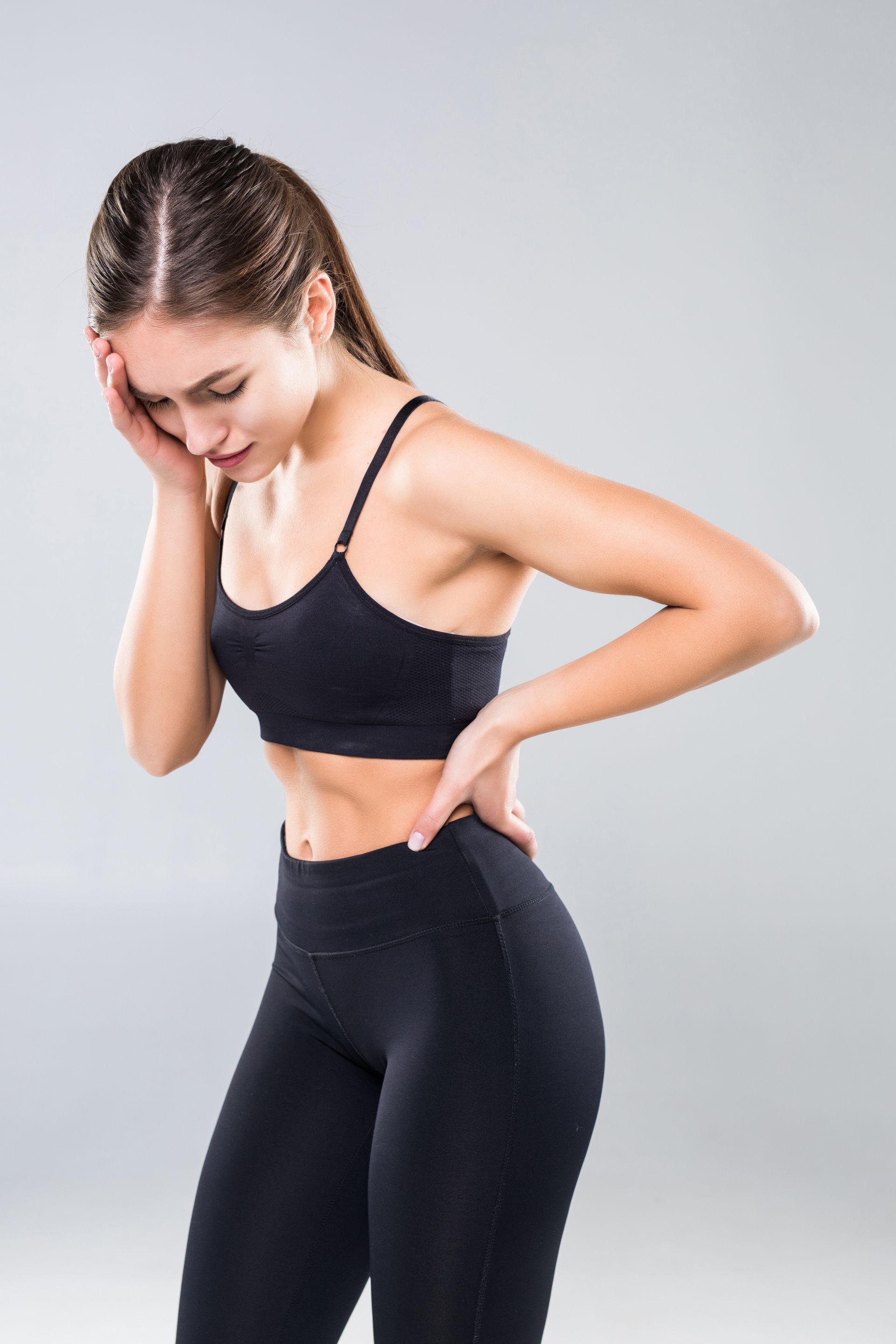 a woman in a sports bra and leggings is holding her back in pain .