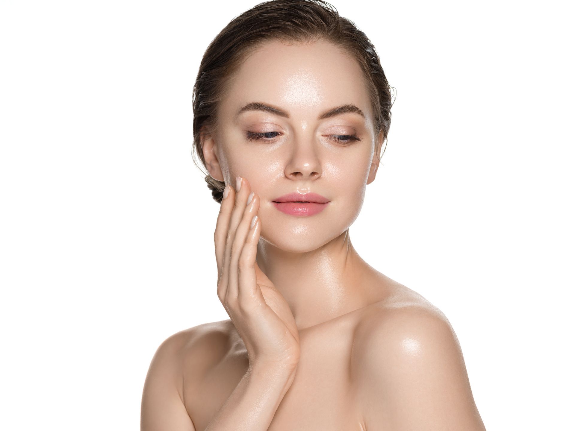 Woman touching cheek, looking down, bright skin, bare shoulders, white background.