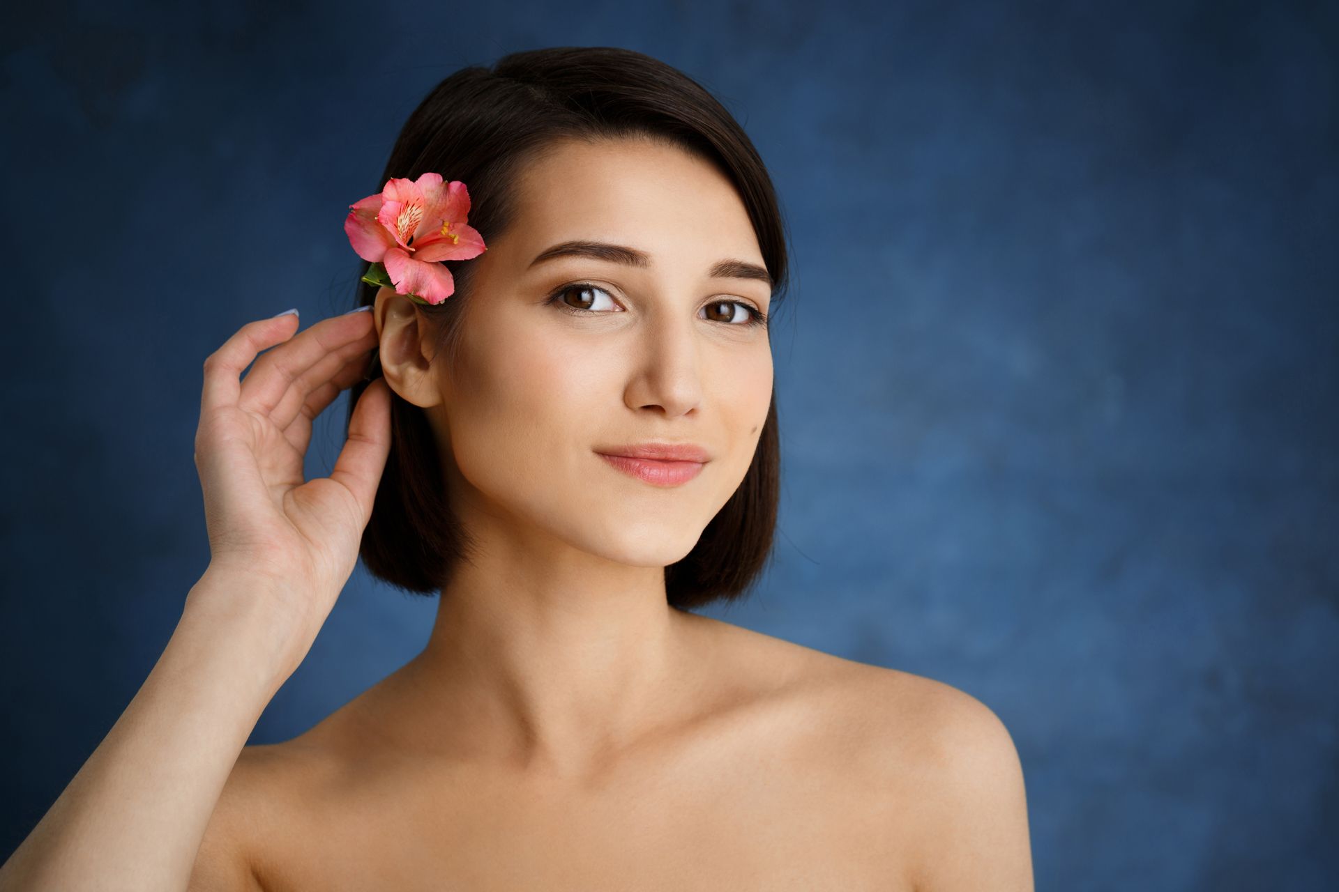 A woman with a flower in her hair is touching her ear.