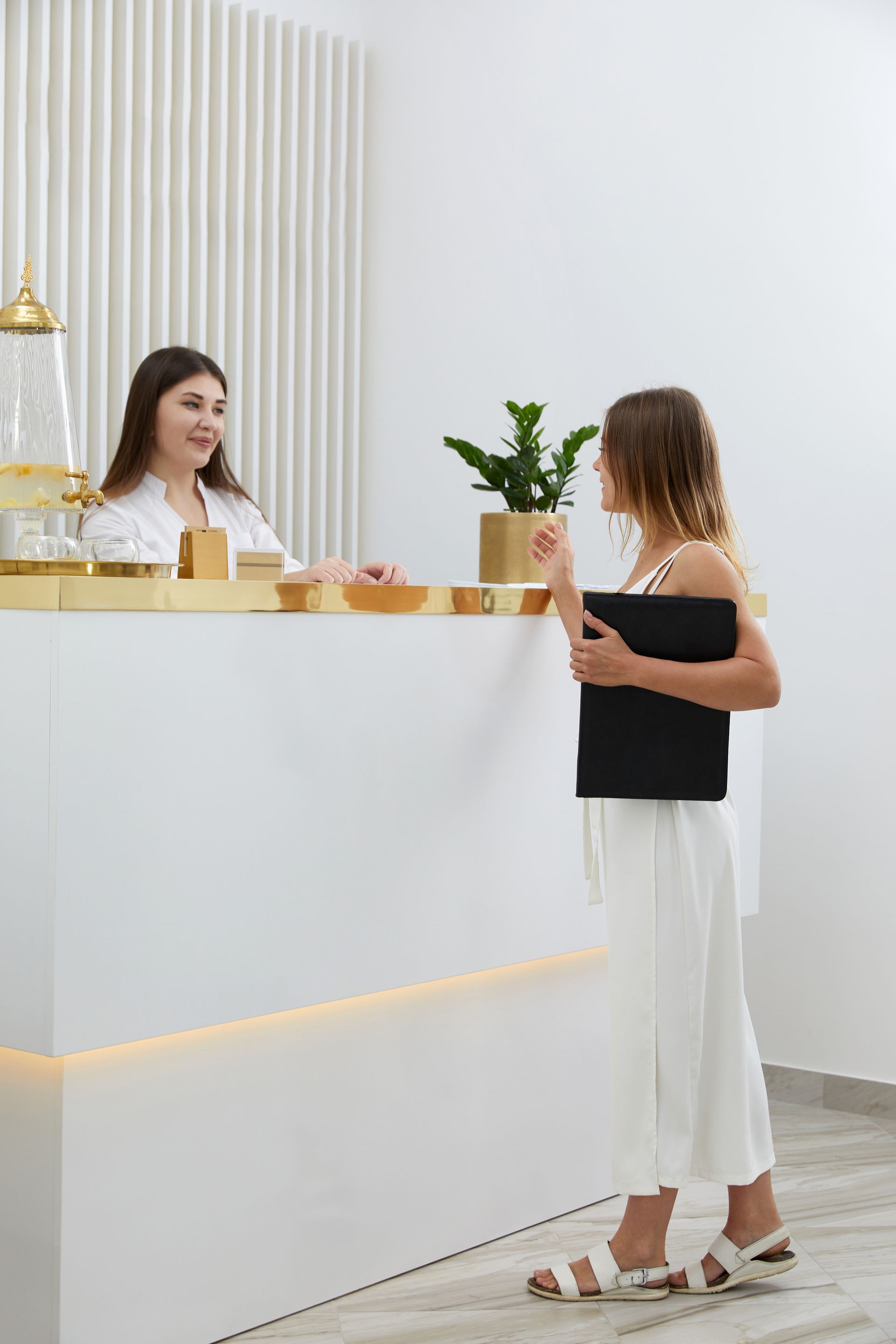 A woman is standing at a reception desk talking to a doctor.