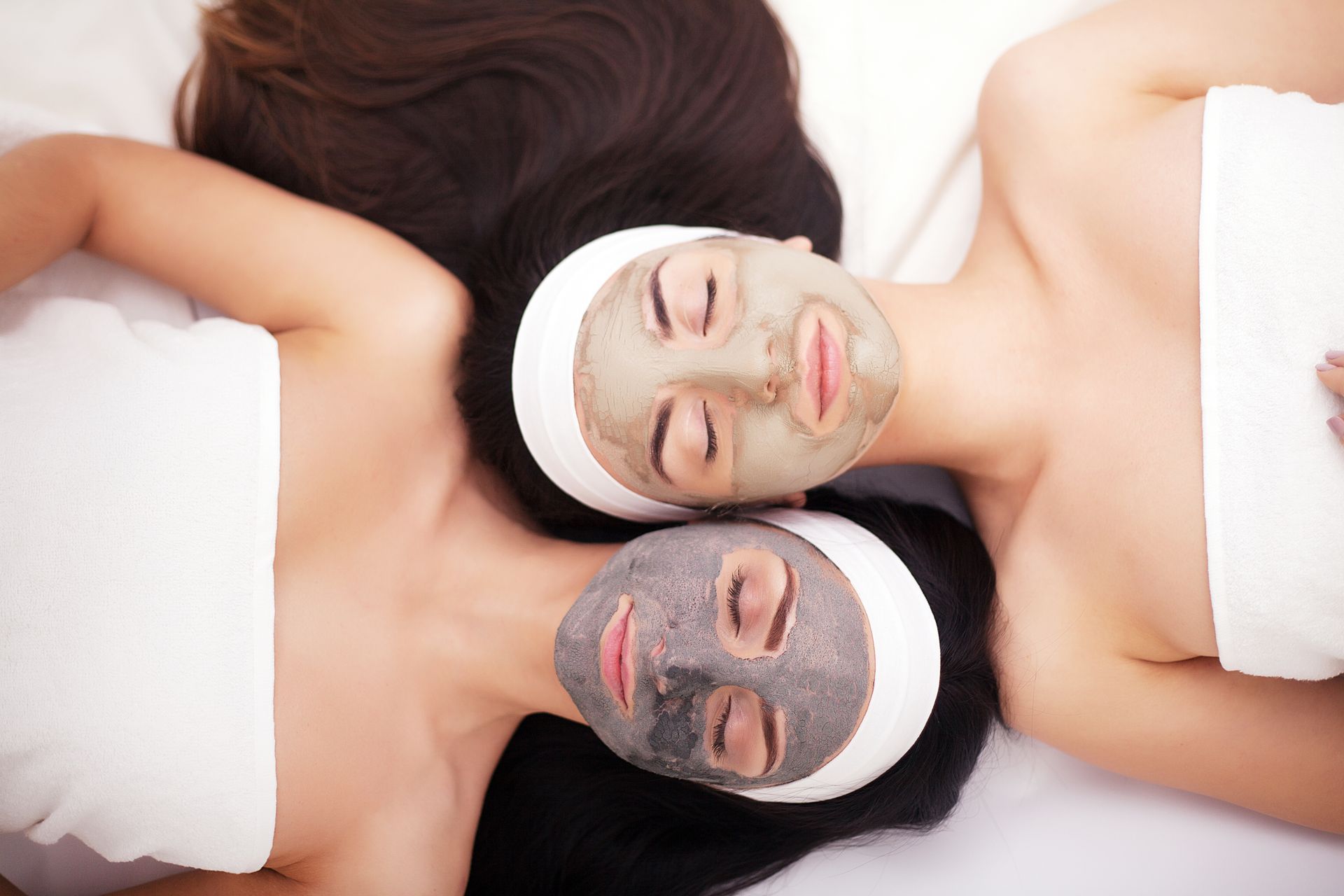 Two people with face masks relaxing, side-by-side, wrapped in white towels.