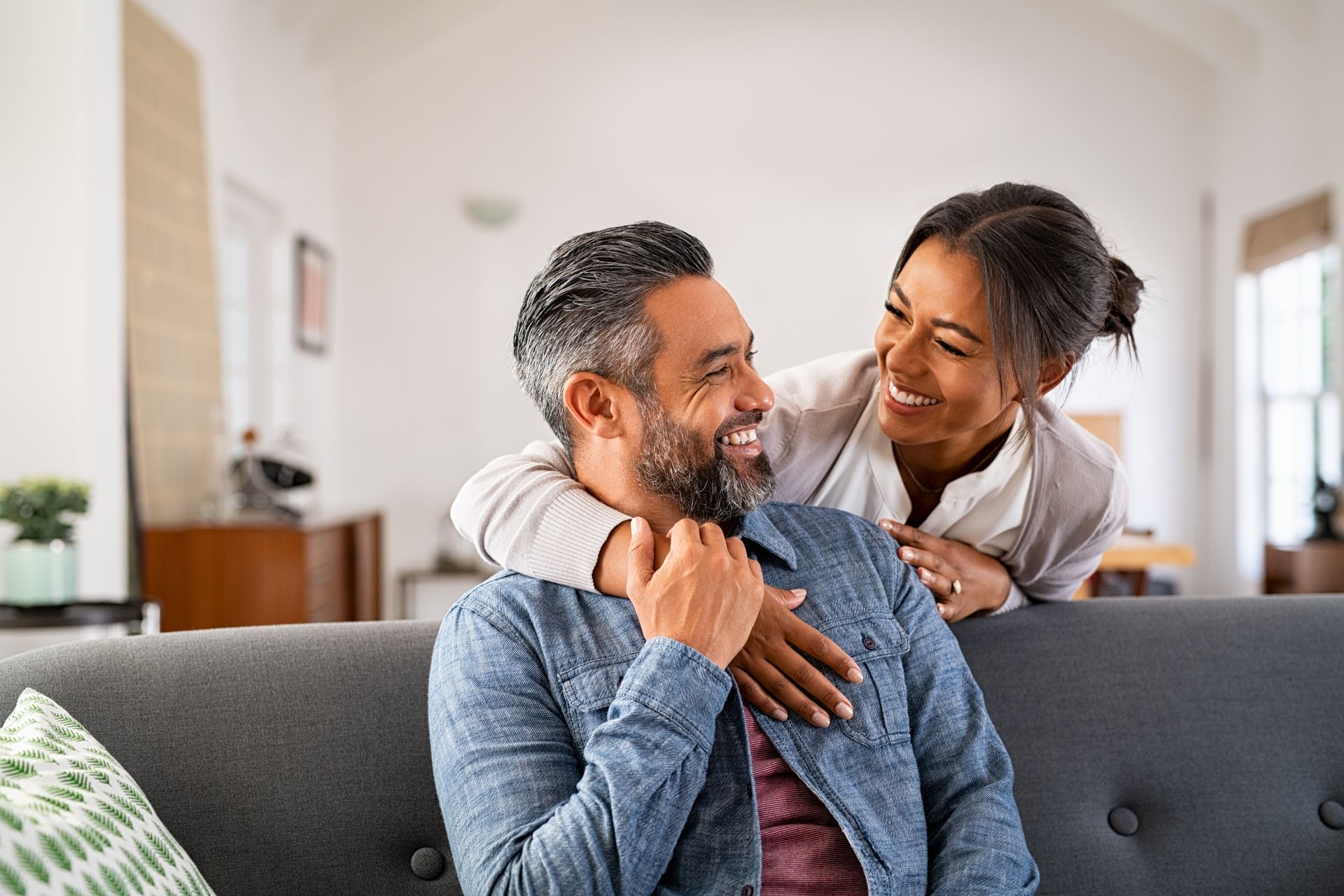 A woman is hugging a man on a couch in a living room.