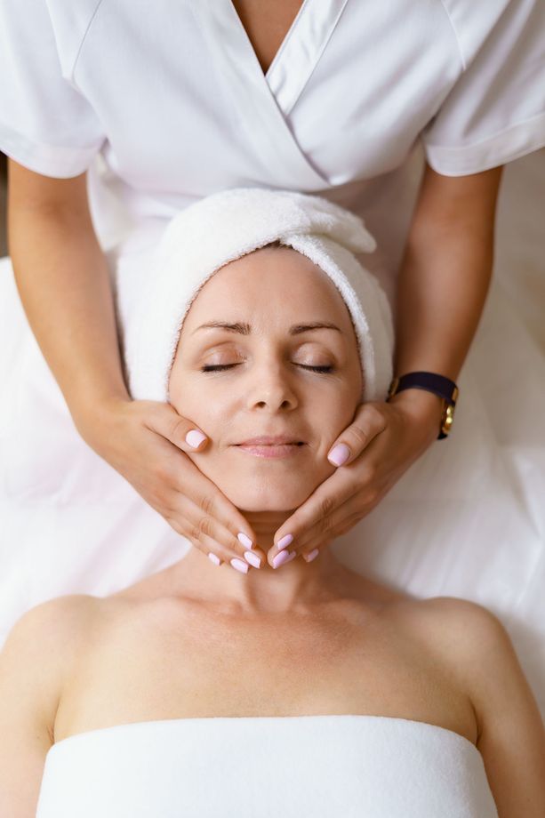 A woman with a towel wrapped around her head is getting a facial massage at a spa.