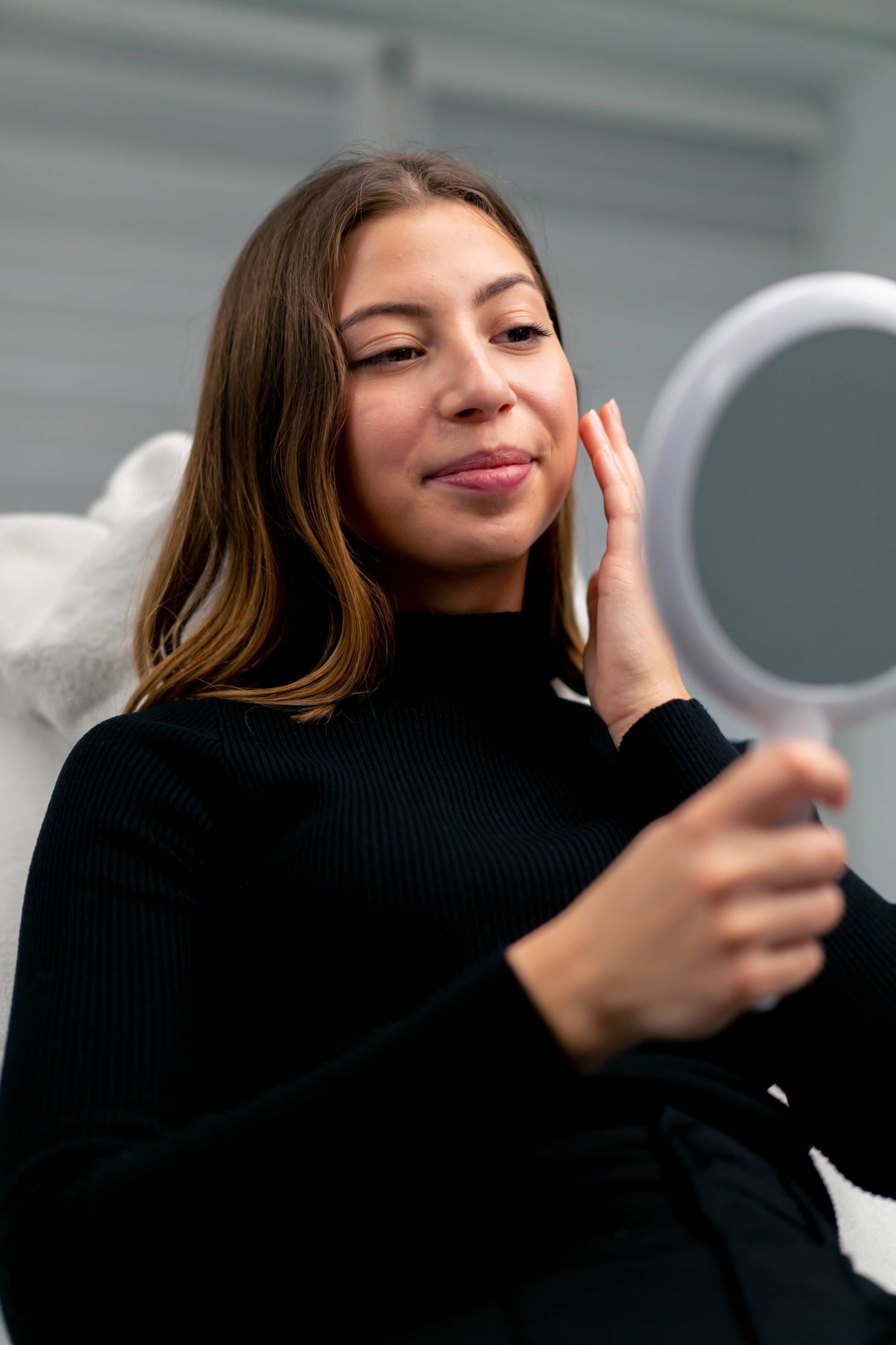 A woman is looking at her face in a mirror.