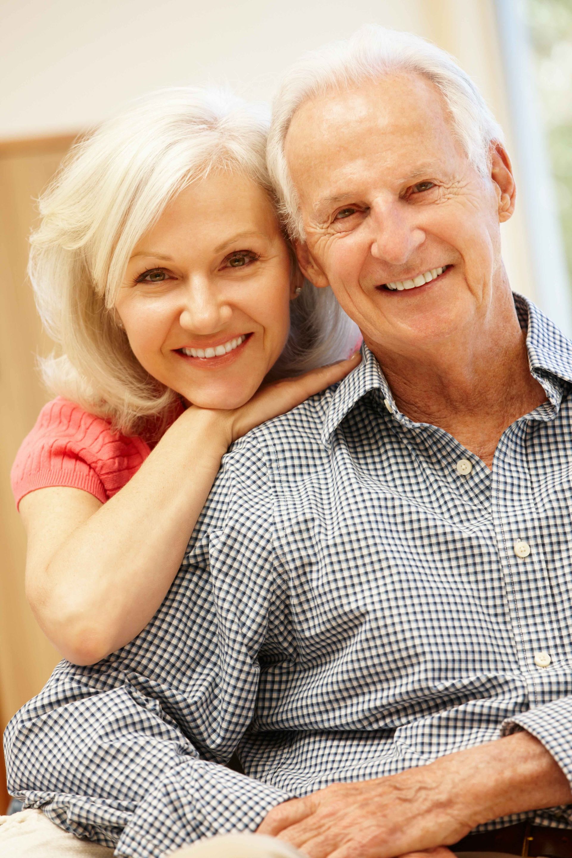 An elderly couple is sitting next to each other and smiling for the camera.