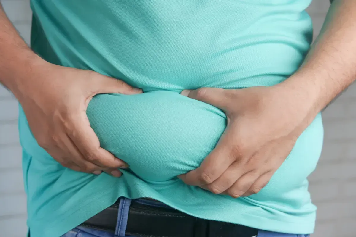 A man in a green shirt is holding his stomach with his hands.