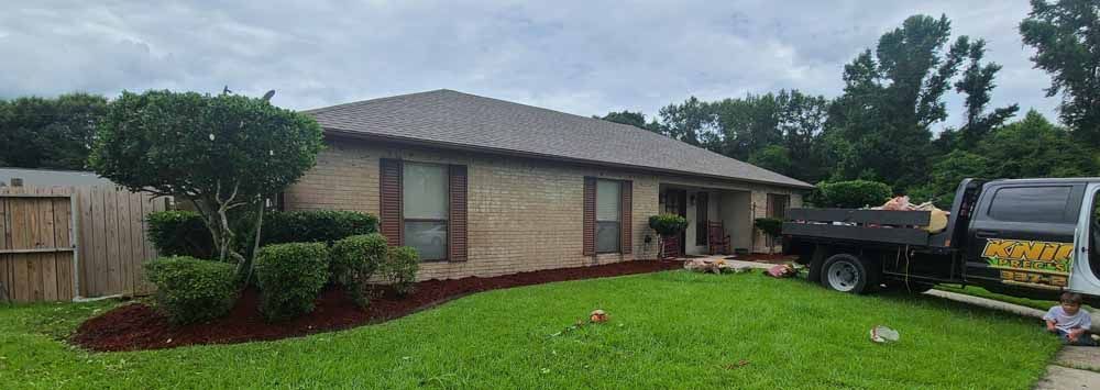 A house with a brown roof and tan brick exterior; a truck is parked on the lawn.