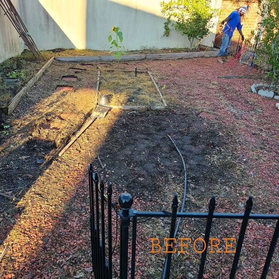 Backyard garden before: man raking in a brown dirt area with a black fence in the foreground and a light-colored wall in the background.