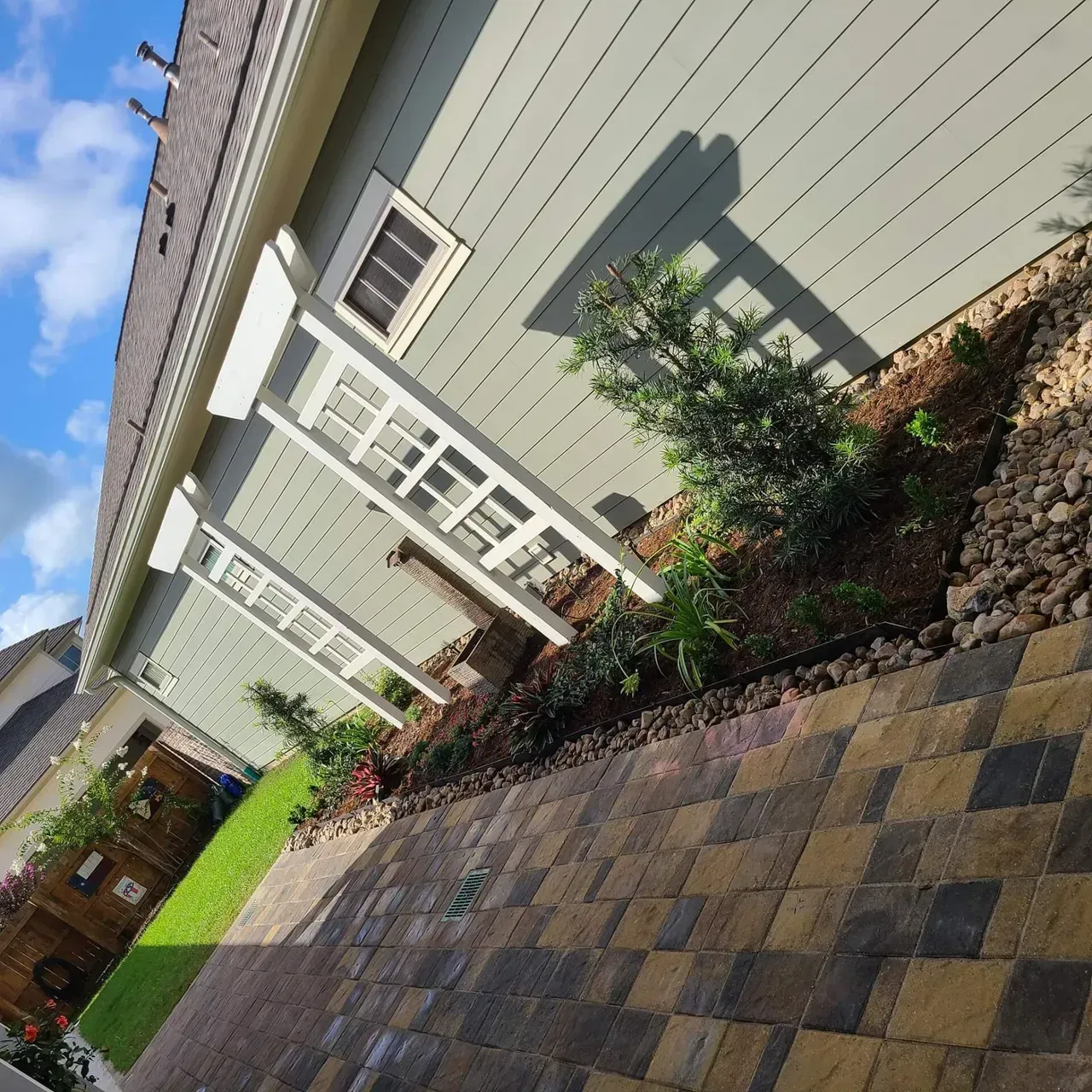House with light green siding, white window trim, and a landscaped garden bed.