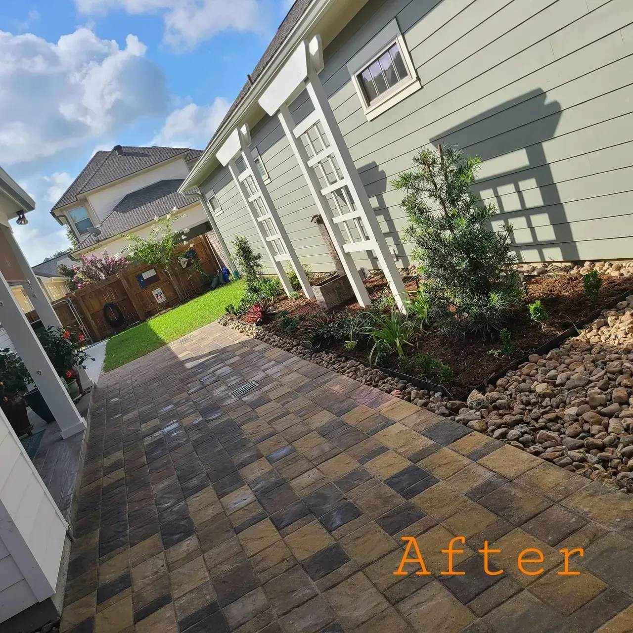 Brick path leads to a garden with green siding and plants. Sky overhead, sunny day.