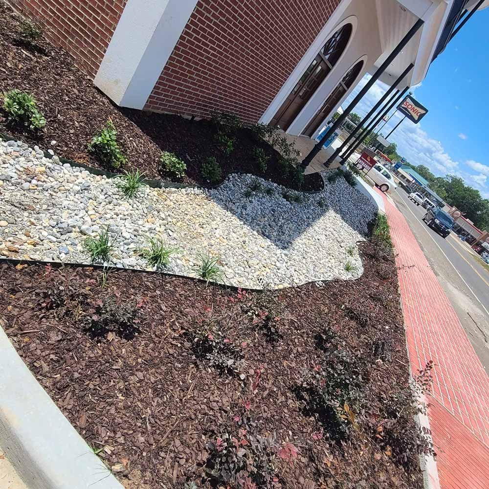Landscaped building front with brick, mulch, and rock beds along a road.
