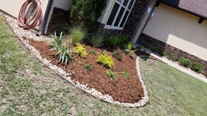 Landscaped flower bed with mulch and stone edging by a house.