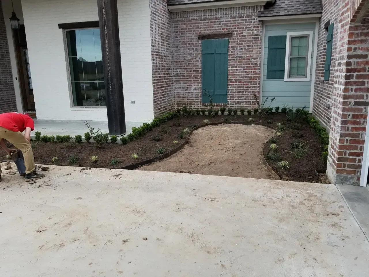 A person planting flowers in a newly made garden bed; a sandy path is in the middle of the garden.