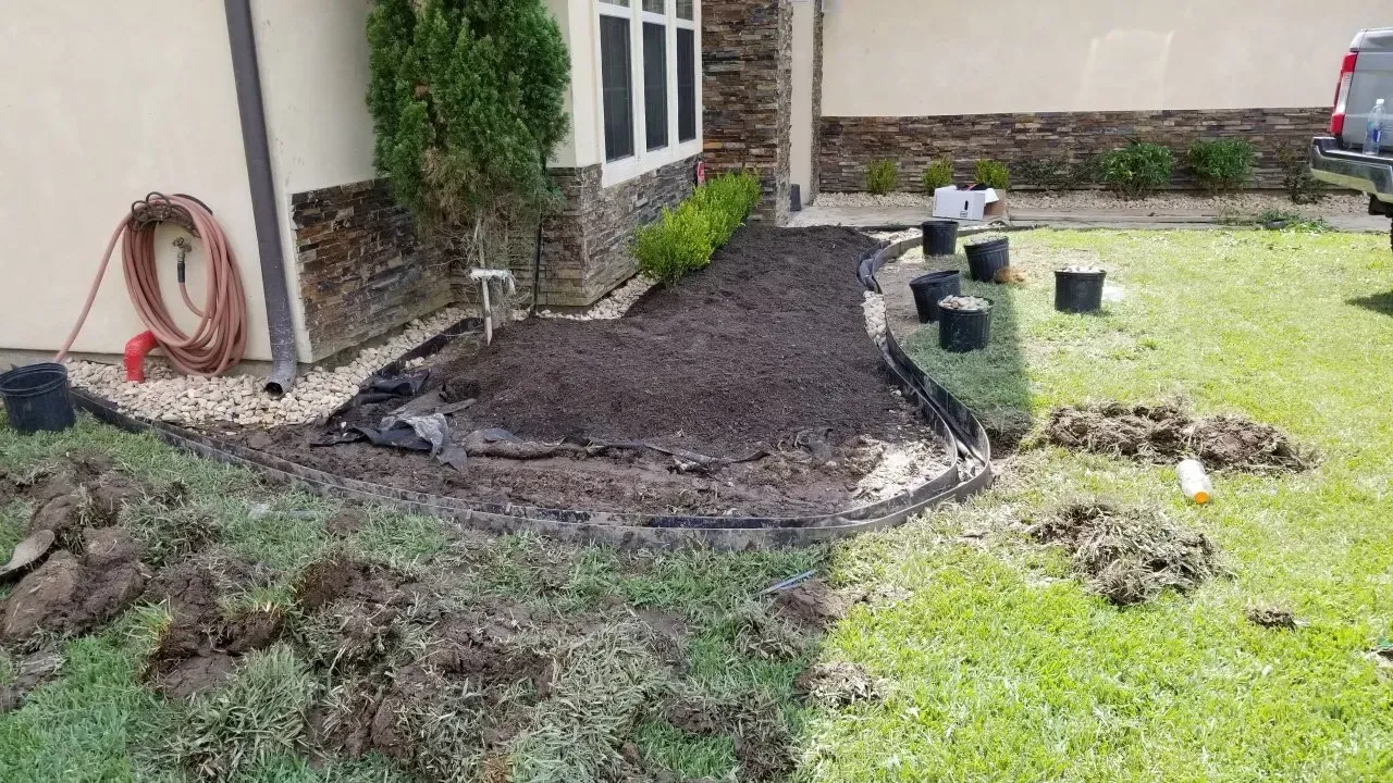 Landscaping in progress; a mulched bed in front of a house, surrounded by grass and work materials.