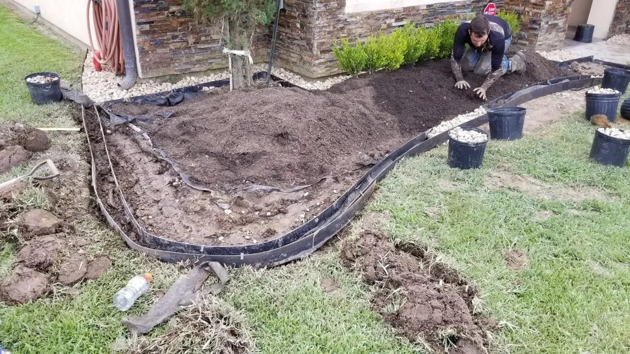 Man adding soil to a garden bed edged with black border on a lawn.