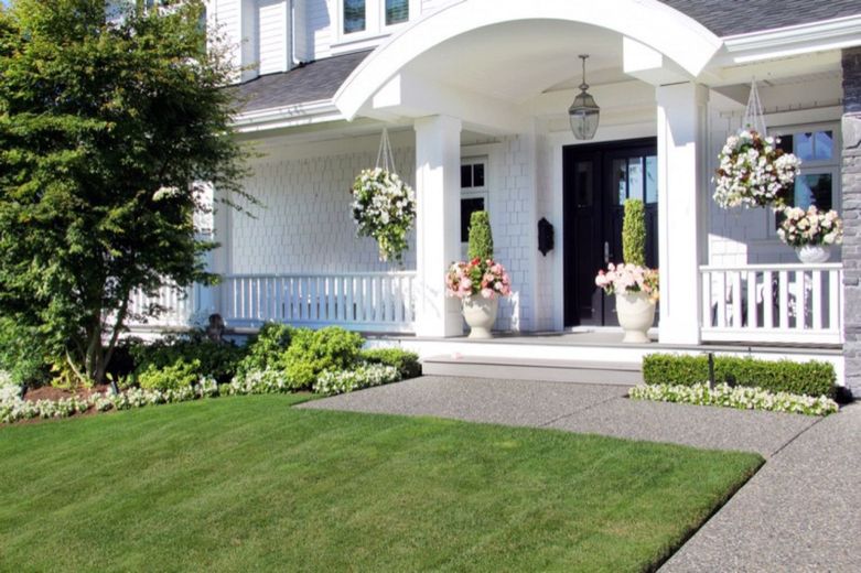 White house with a porch, lush green lawn, and flower baskets hanging.