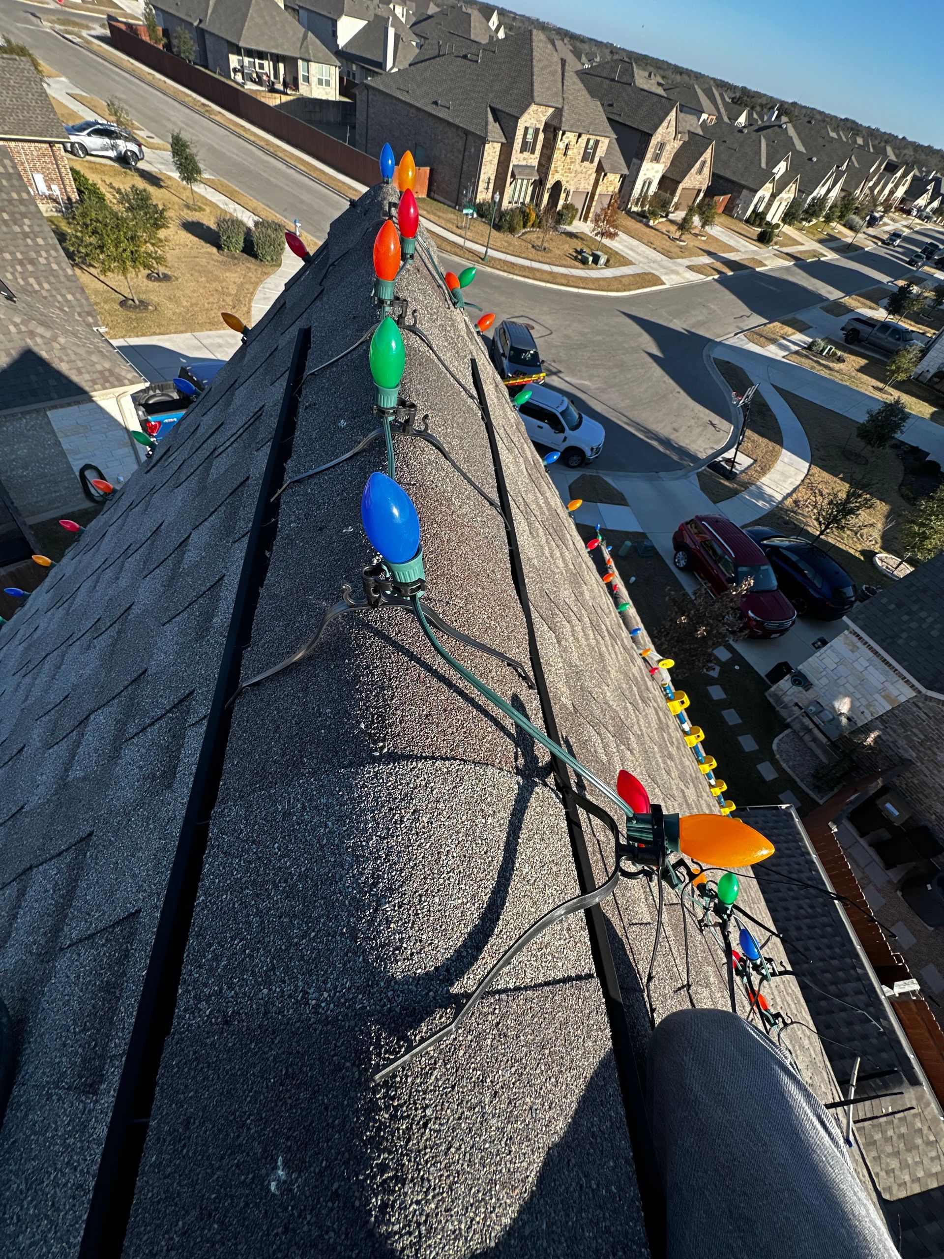Christmas lights strung along a dark rooftop with a neighborhood in the background.