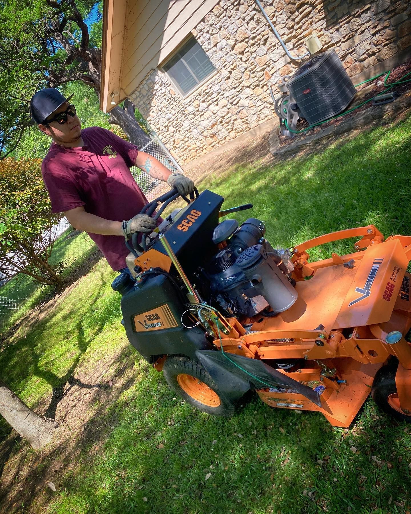 Person operating an orange riding mower on a grassy lawn beside a stone house.