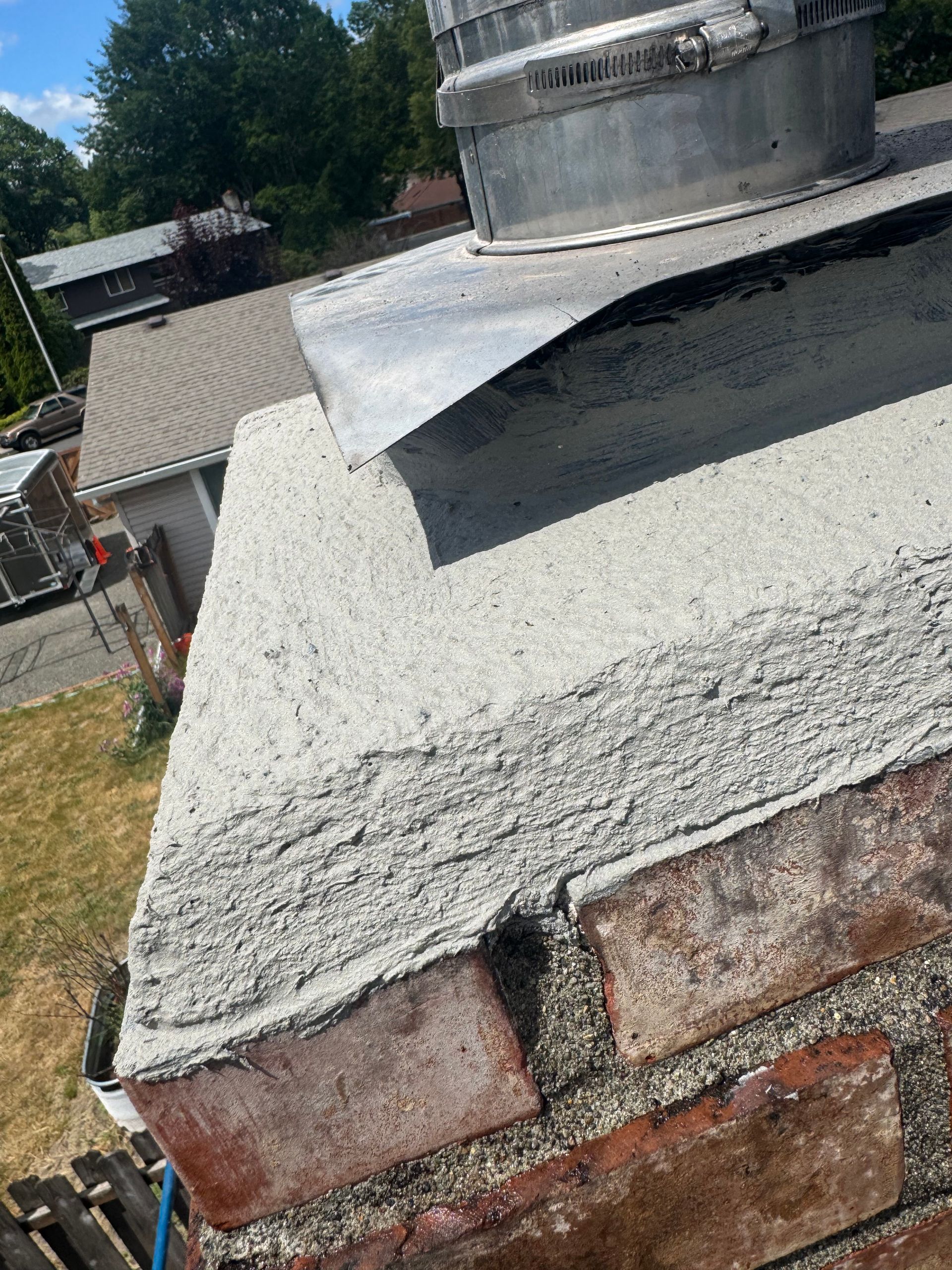 Close-up of a brick chimney with new concrete crown, metal flashing, and cap.