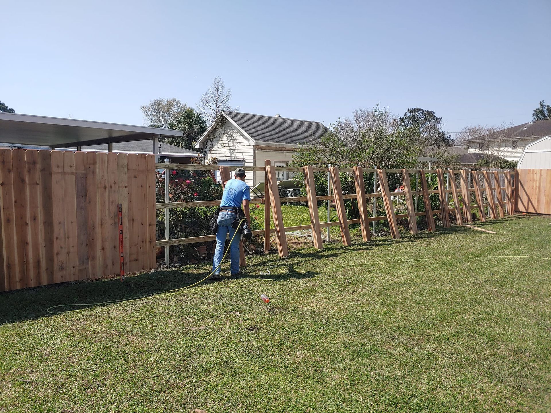 A man is standing in front of a wooden fence in a yard.
