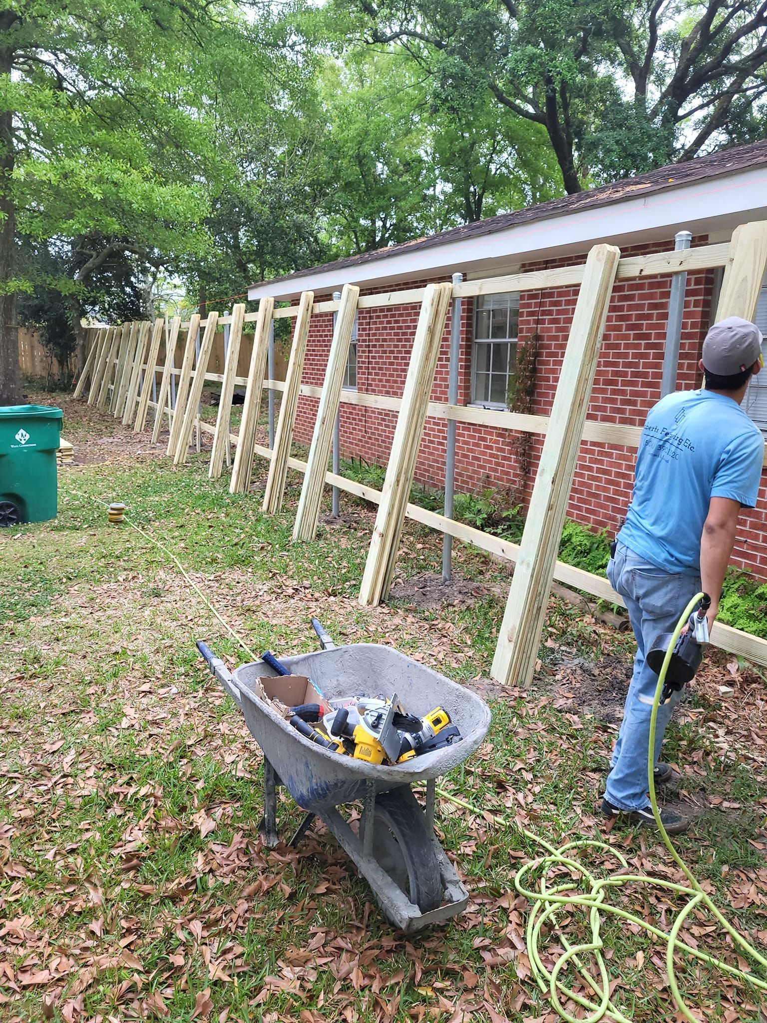 A man is standing next to a wheelbarrow filled with tools in front of a brick building.