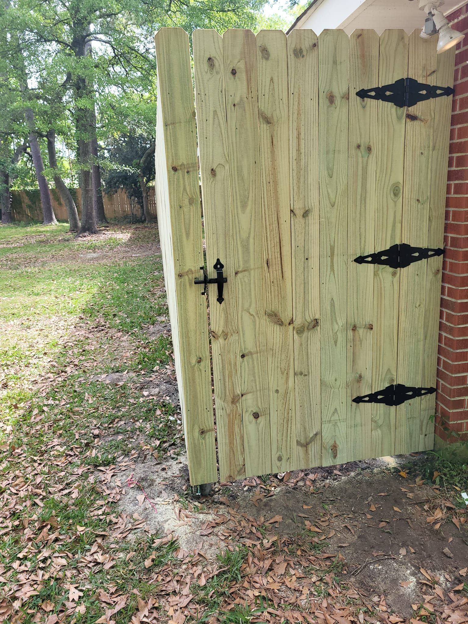A wooden gate with black hinges is sitting next to a brick building.