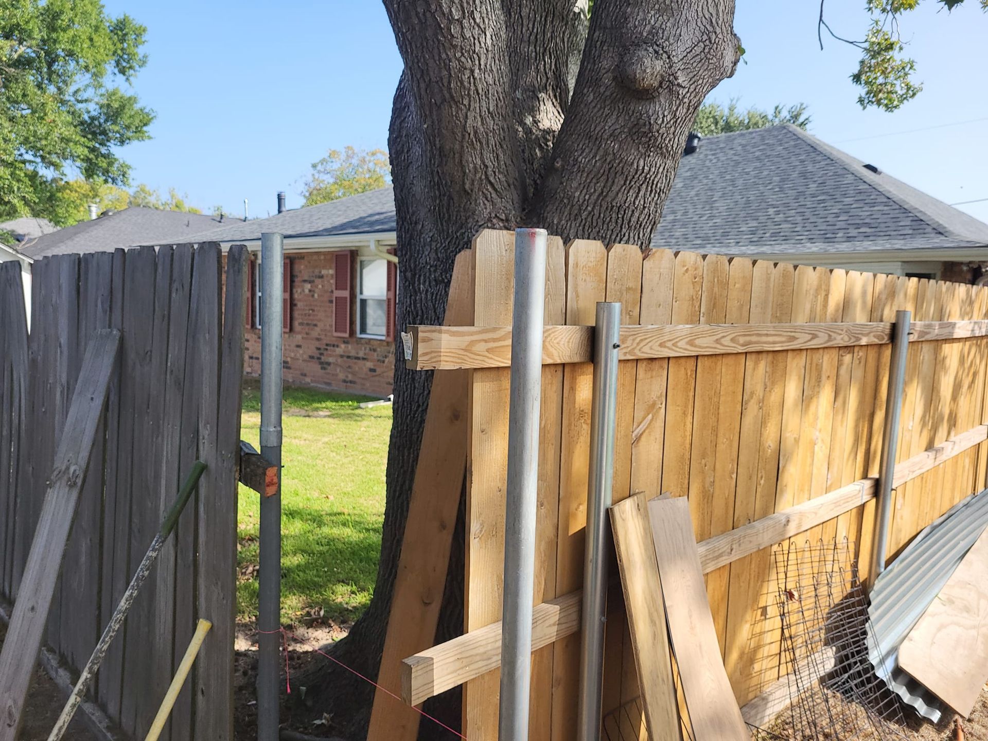 A wooden fence is being built next to a tree in front of a house.