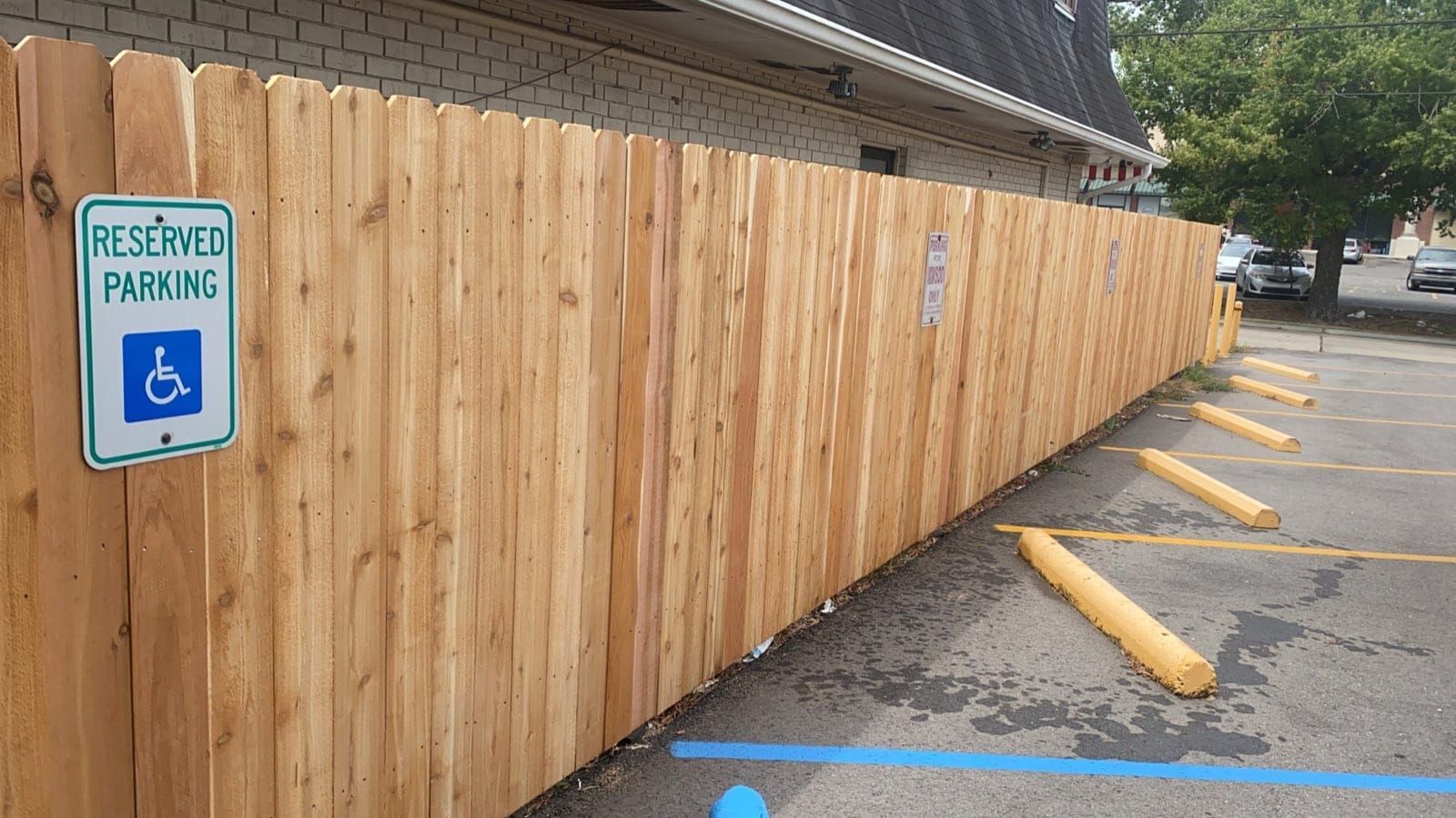 A wooden fence surrounds a parking lot with a handicapped parking sign.