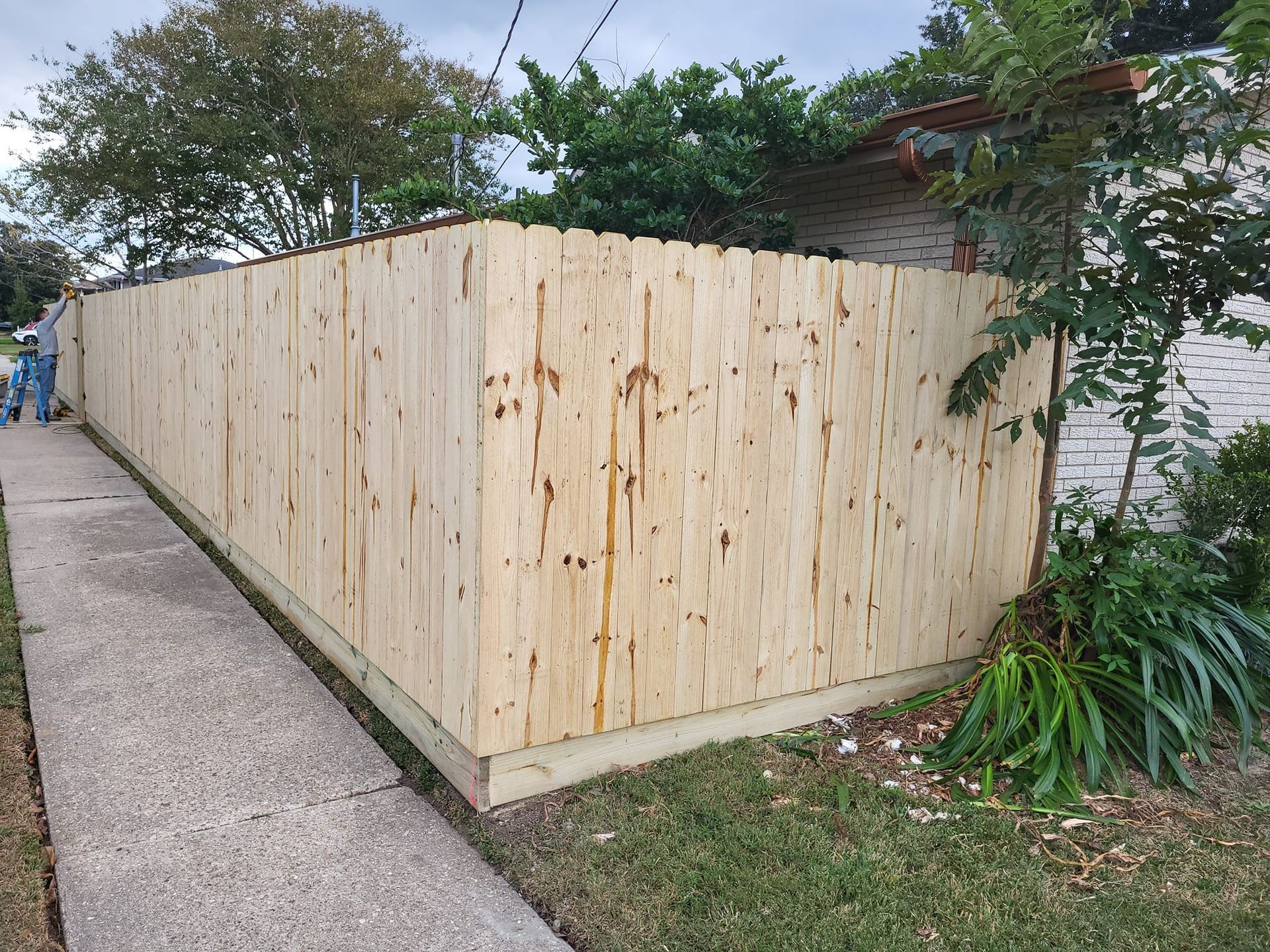 A wooden fence is sitting on the side of a sidewalk next to a house.