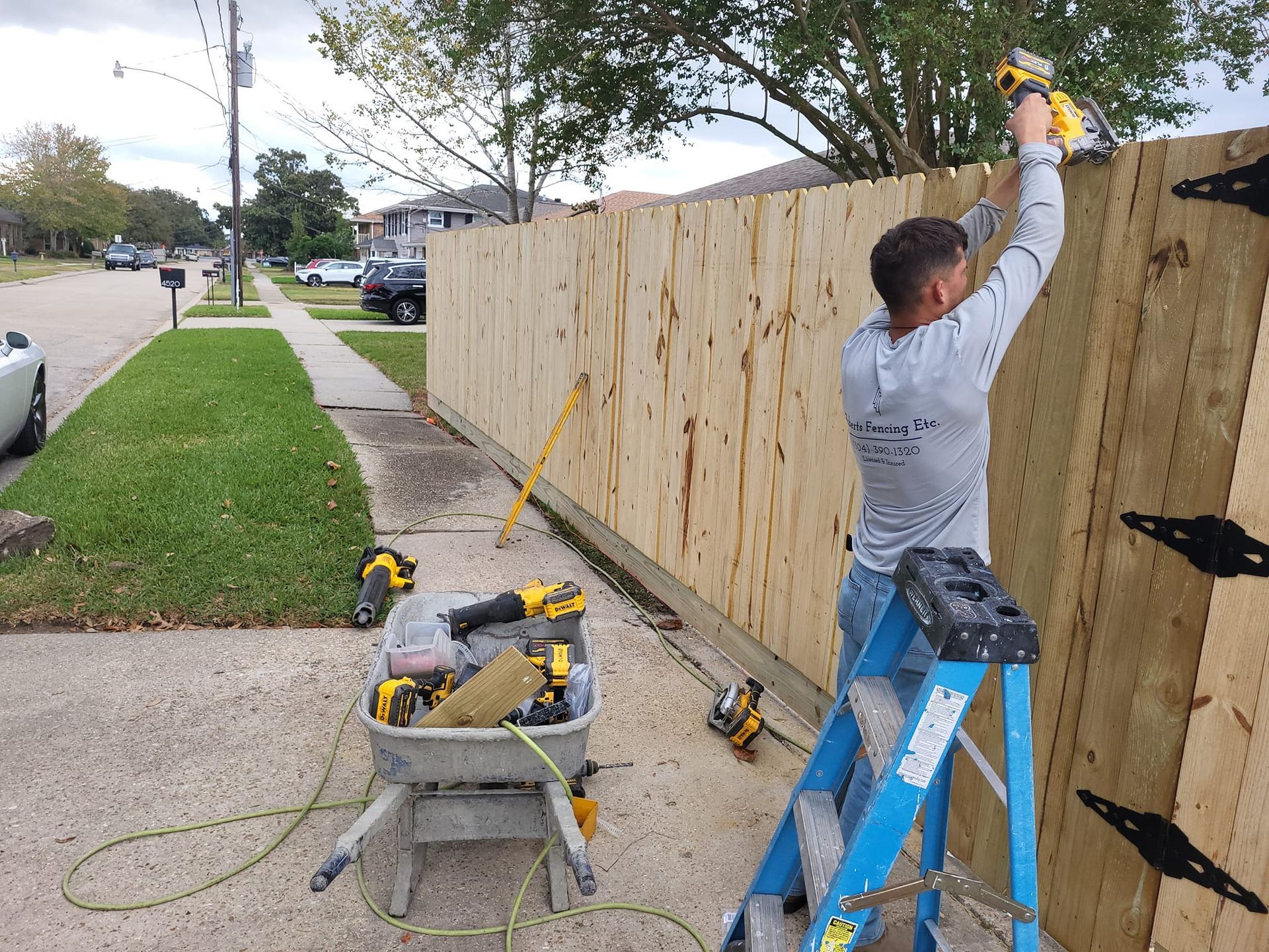 A man is standing on a ladder fixing a wooden fence.