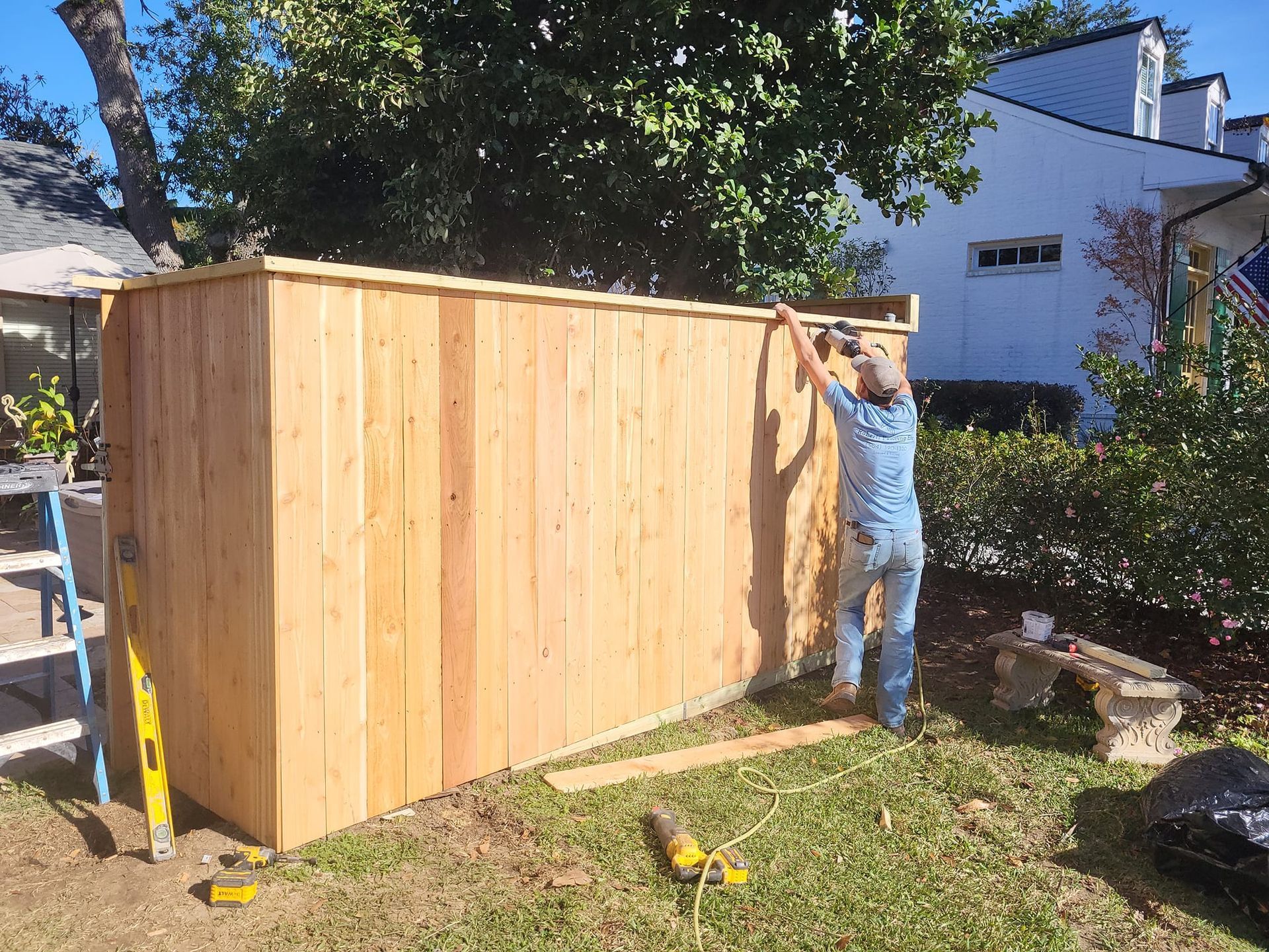 A man is working on a wooden fence in a backyard.