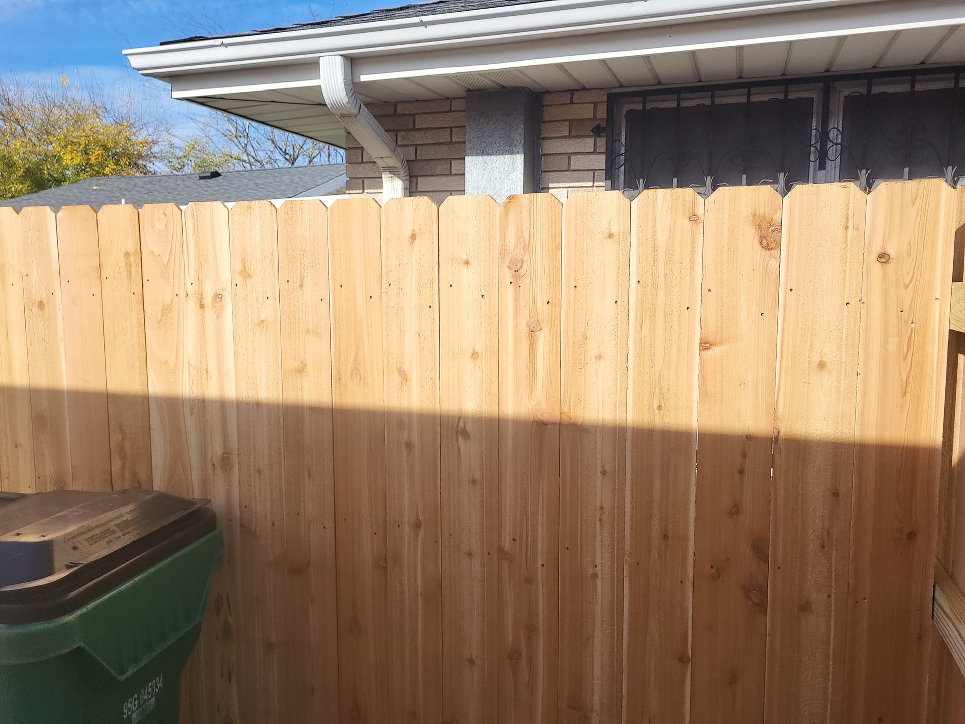 A wooden fence with a green trash can in front of it.