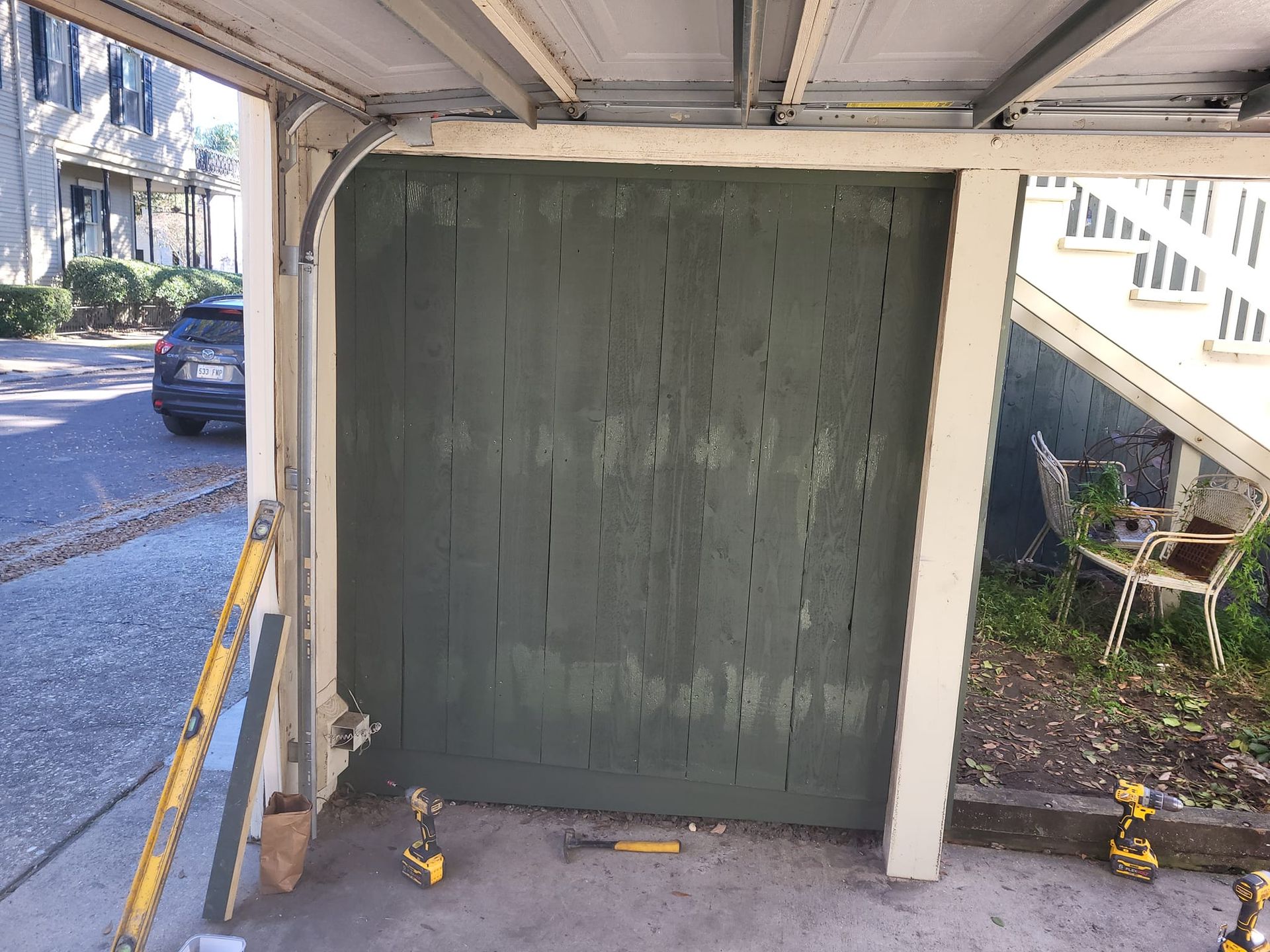 A garage door is being repaired with tools and a car parked in the background.