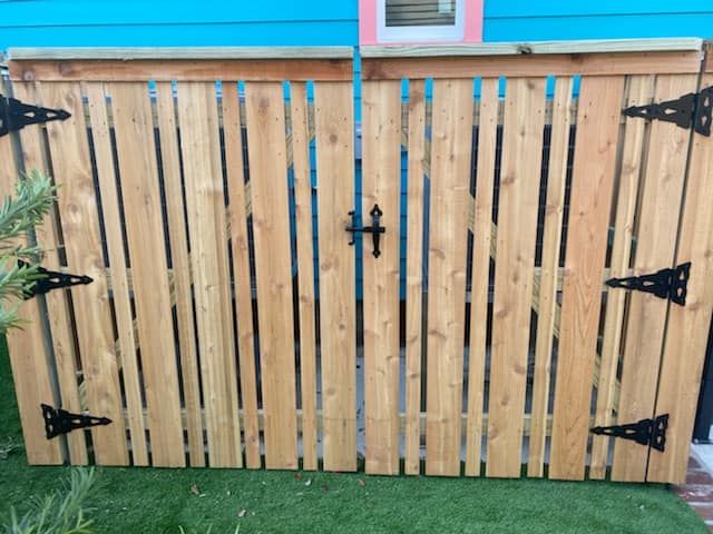 A wooden fence with black hinges is sitting on top of a lush green lawn.