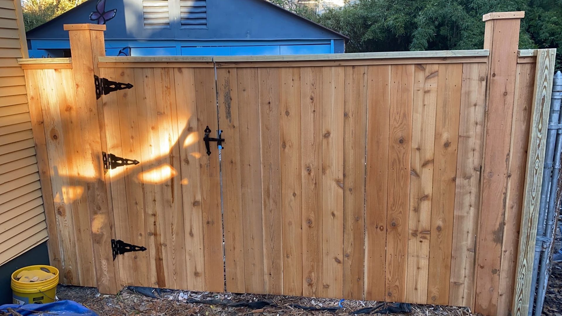 A wooden fence with a gate and a blue garage in the background